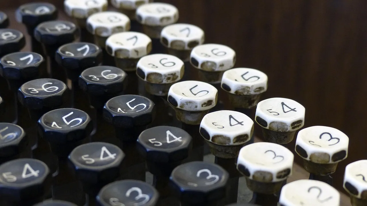 A close view of the worn, eight-sided number keys of an old adding machine, in columns of black keys and cream keys, each key marked with a large digit and a smaller second figure.