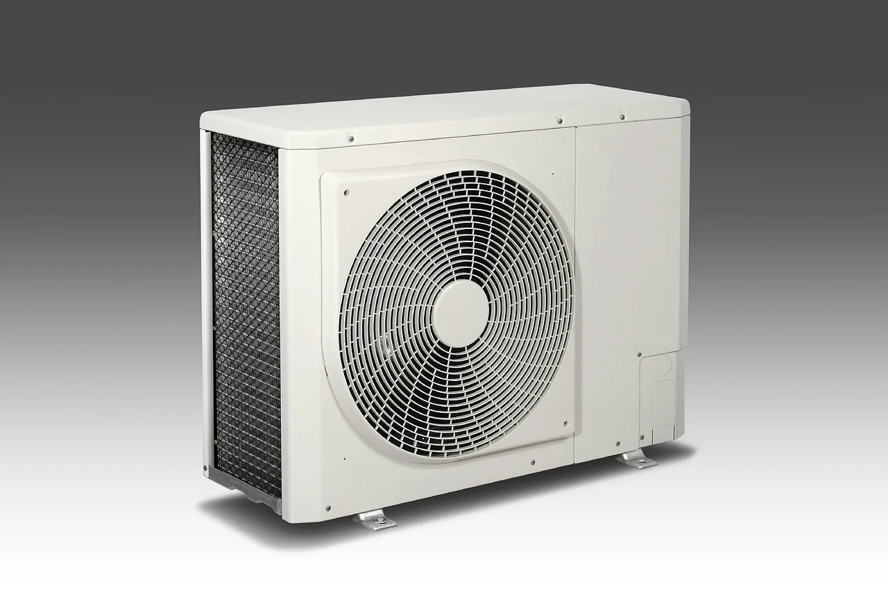 A plain white outdoor air conditioner unit with a round fan grille, photographed against a grey background