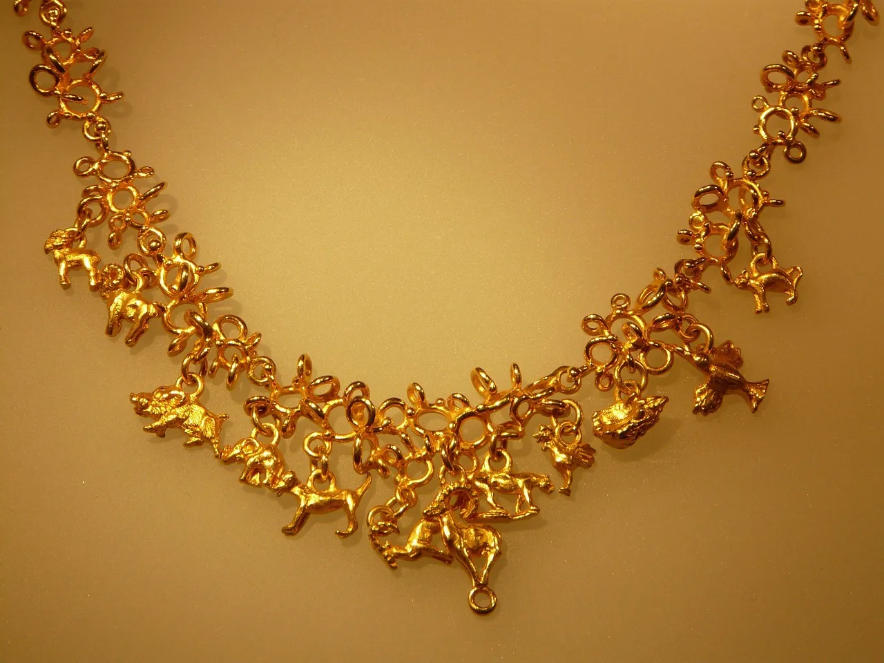 A gold-coloured necklace hung with small animal charms, lit warmly against a plain background.