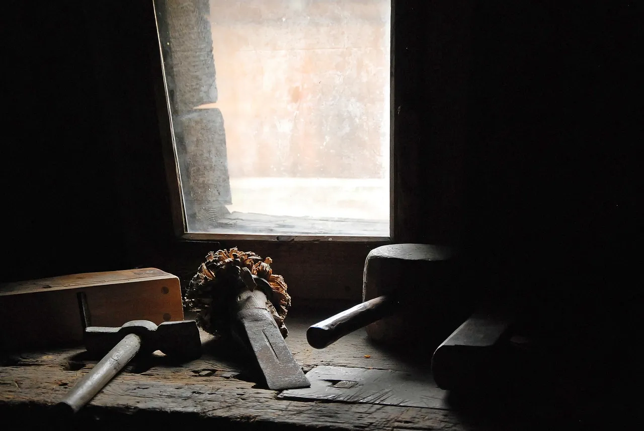 Old hand tools, including a wooden mallet and a hammer, resting on a workbench in the light of a small window