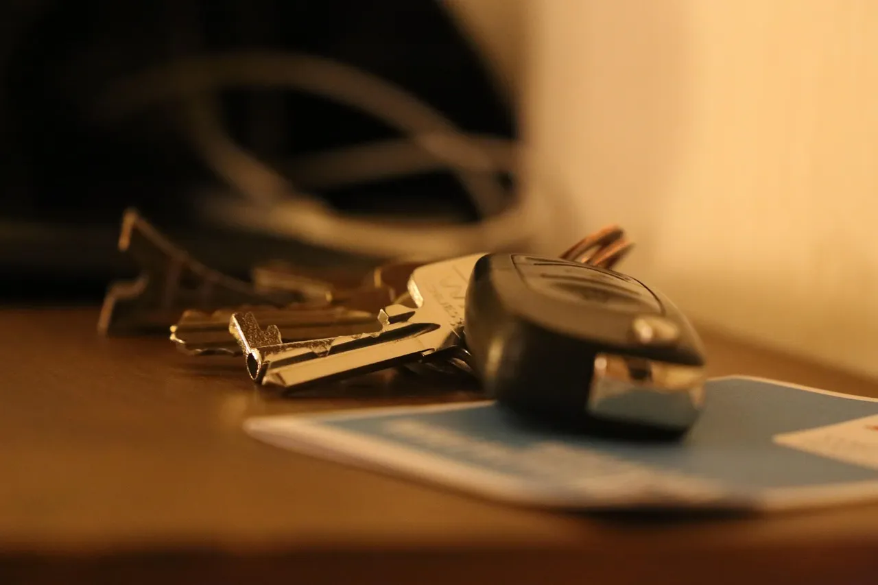 A bunch of car keys with a remote key fob resting on a pale blue folded document, on a wooden surface in warm lamplight
