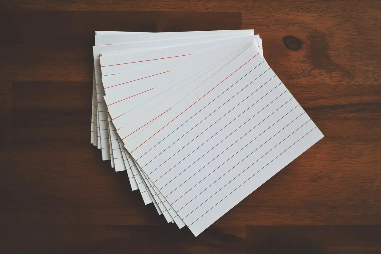 A fan of blank ruled index cards, each with a red line across the top, on a dark timber desk.
