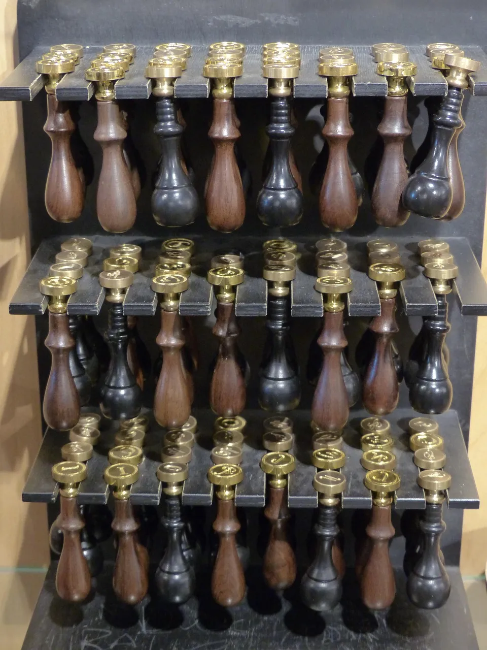 Rows of wooden-handled brass seal stamps standing in a black rack.