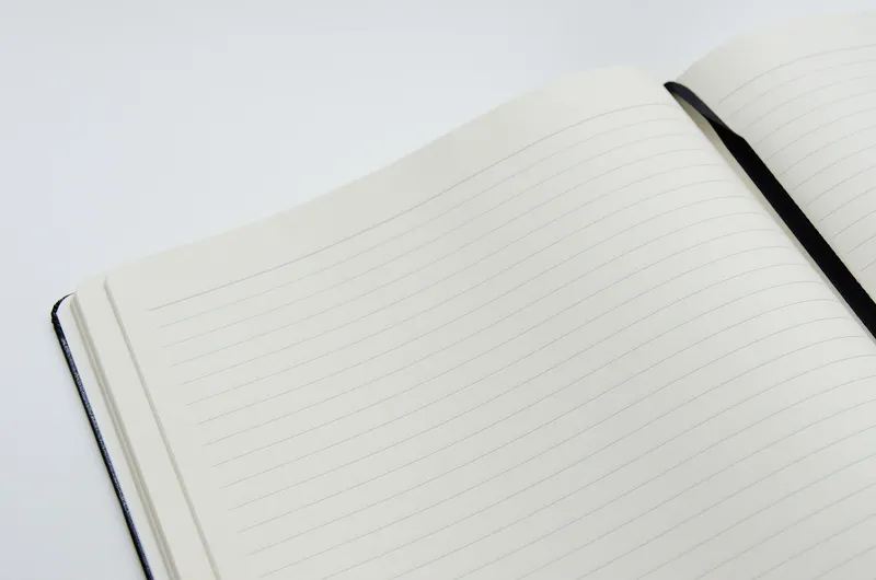 An open notebook with blank ruled pages and a black ribbon marker lying across the page.