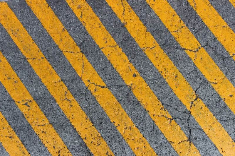 Yellow diagonal hazard stripes painted on a cracked grey concrete surface