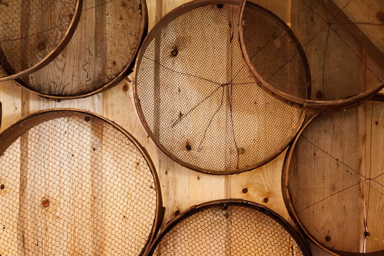 Several old round sieves with dark rims, each with a different wire mesh, hung on a pale timber wall