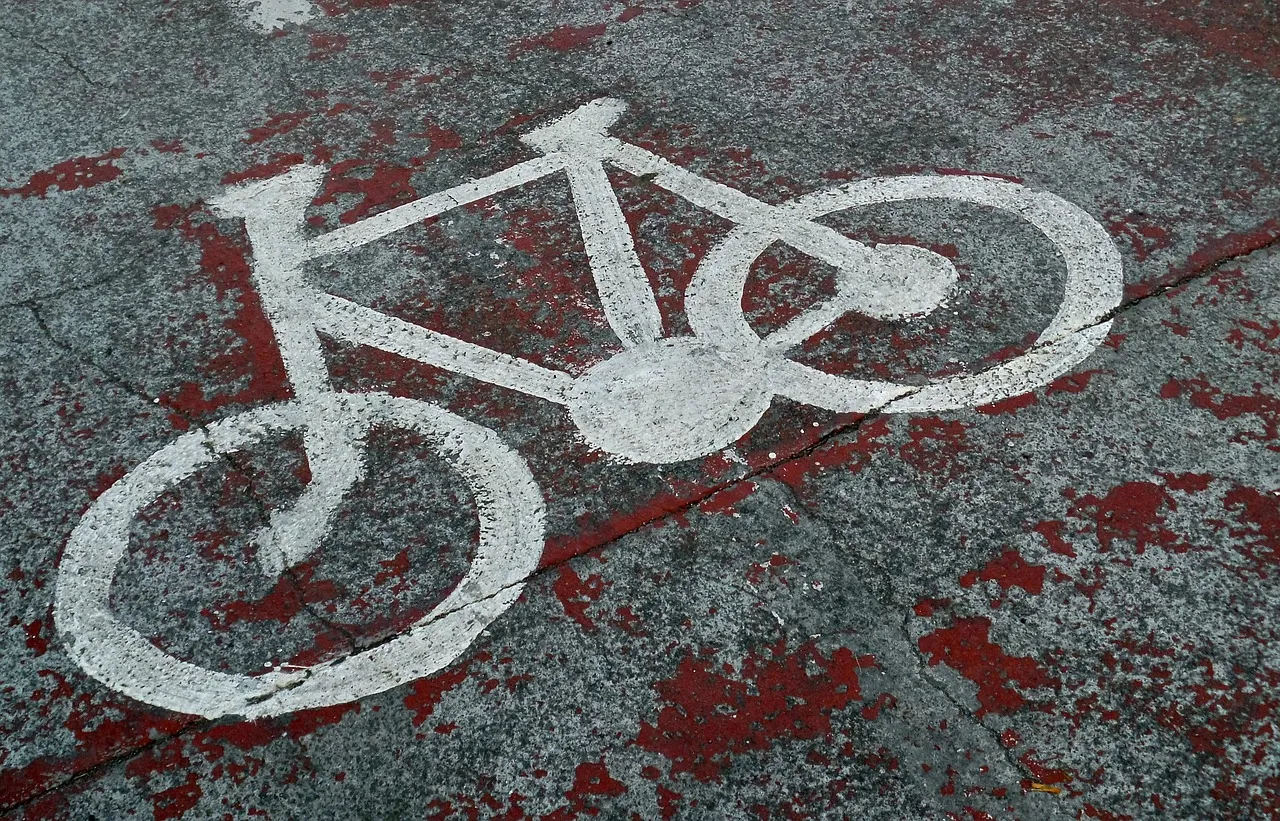 A white bicycle symbol painted on grey asphalt, over patches of worn red paint.
