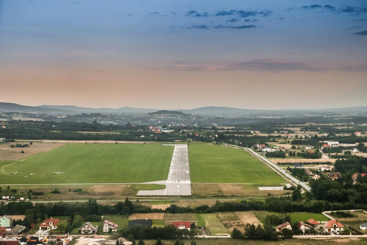 A runway seen from the air on its approach line, with fields either side and houses beneath the approach