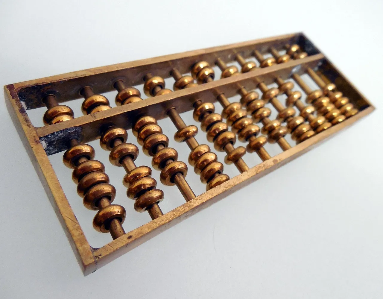 A small brass abacus lying at an angle on a white surface, its beads stacked on short rods either side of a crossbar.
