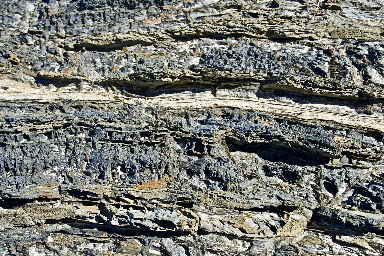 A weathered rock face in horizontal layers of grey, cream and rust-coloured stone.