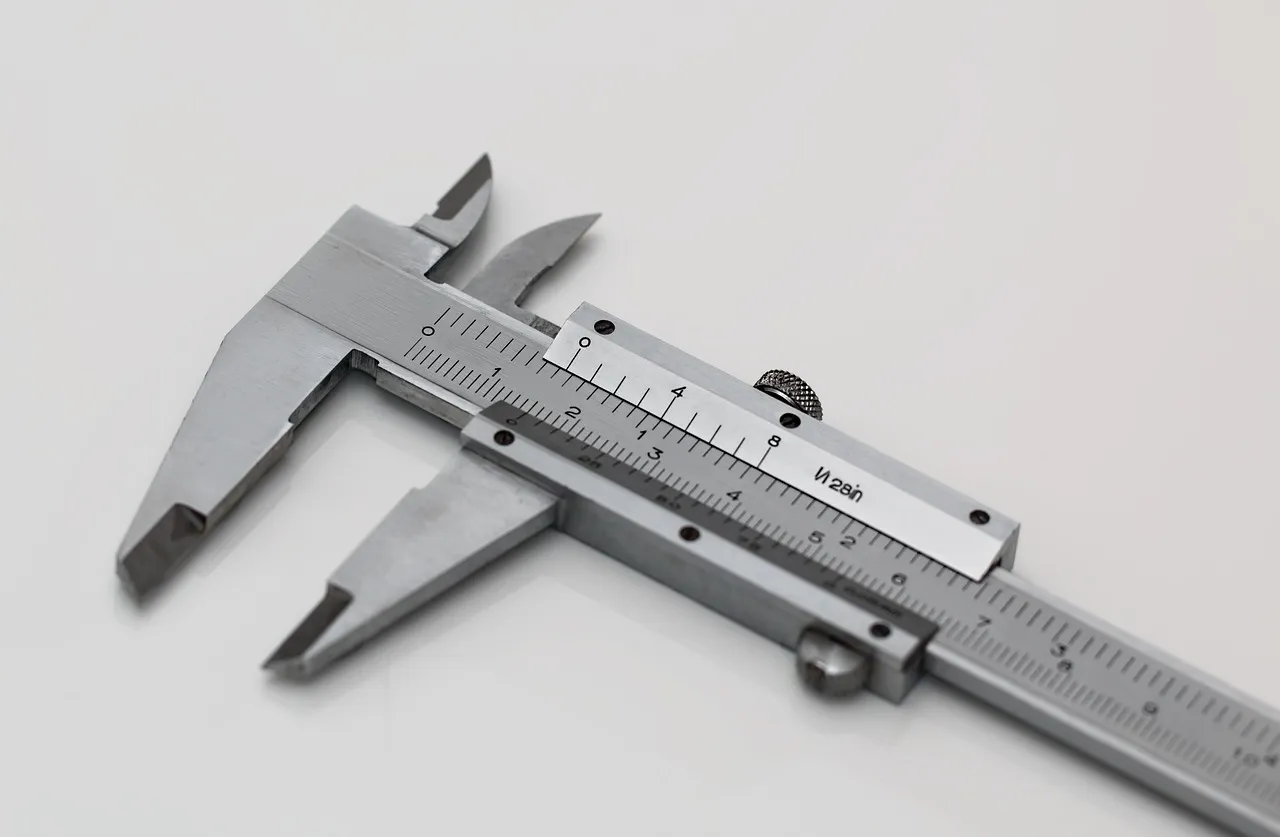 A steel vernier caliper on a pale surface, its main scale and sliding vernier scale marked in fine lines.