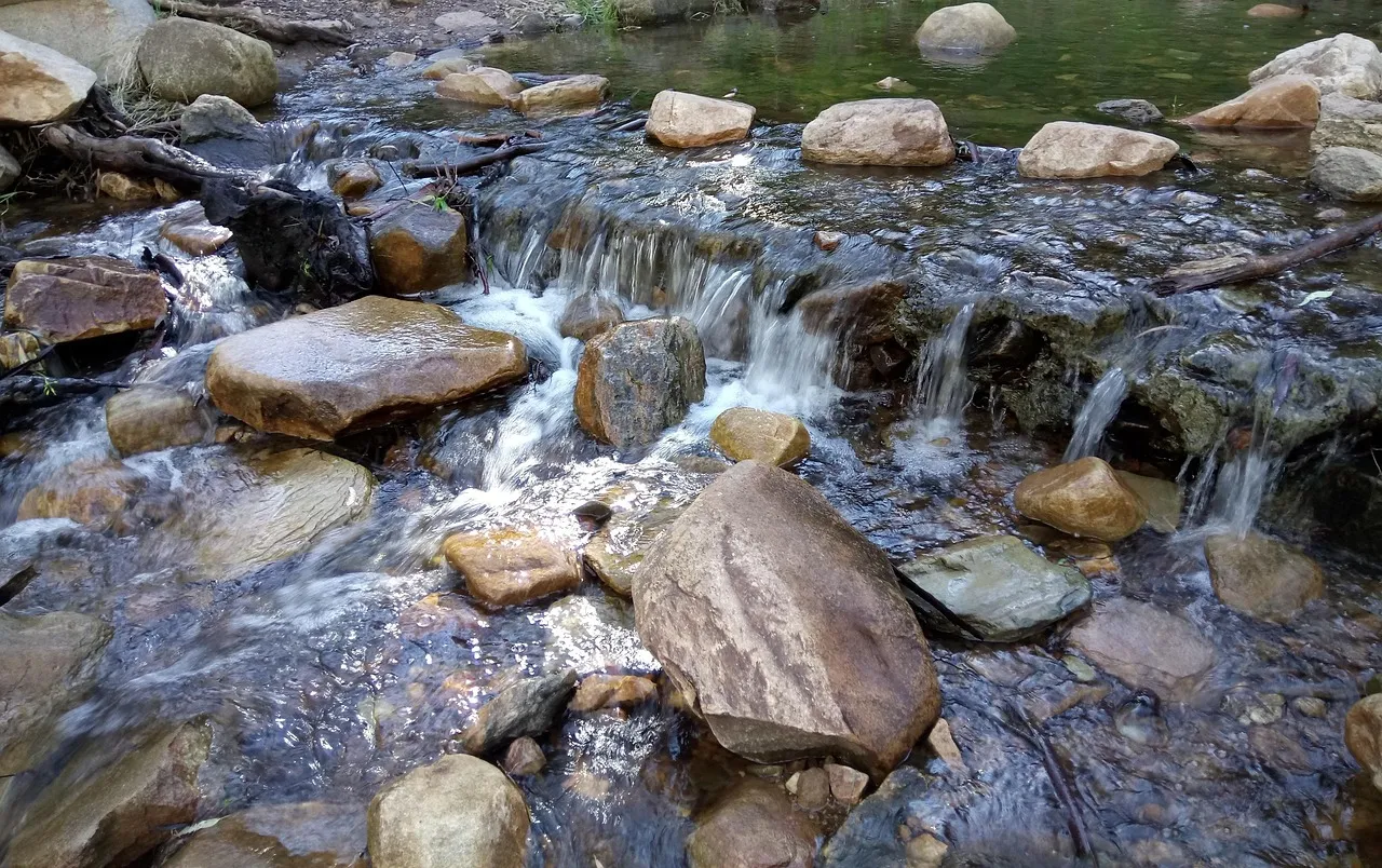 Smooth rounded stones in a shallow creek, with clear water running over a low rock ledge between them