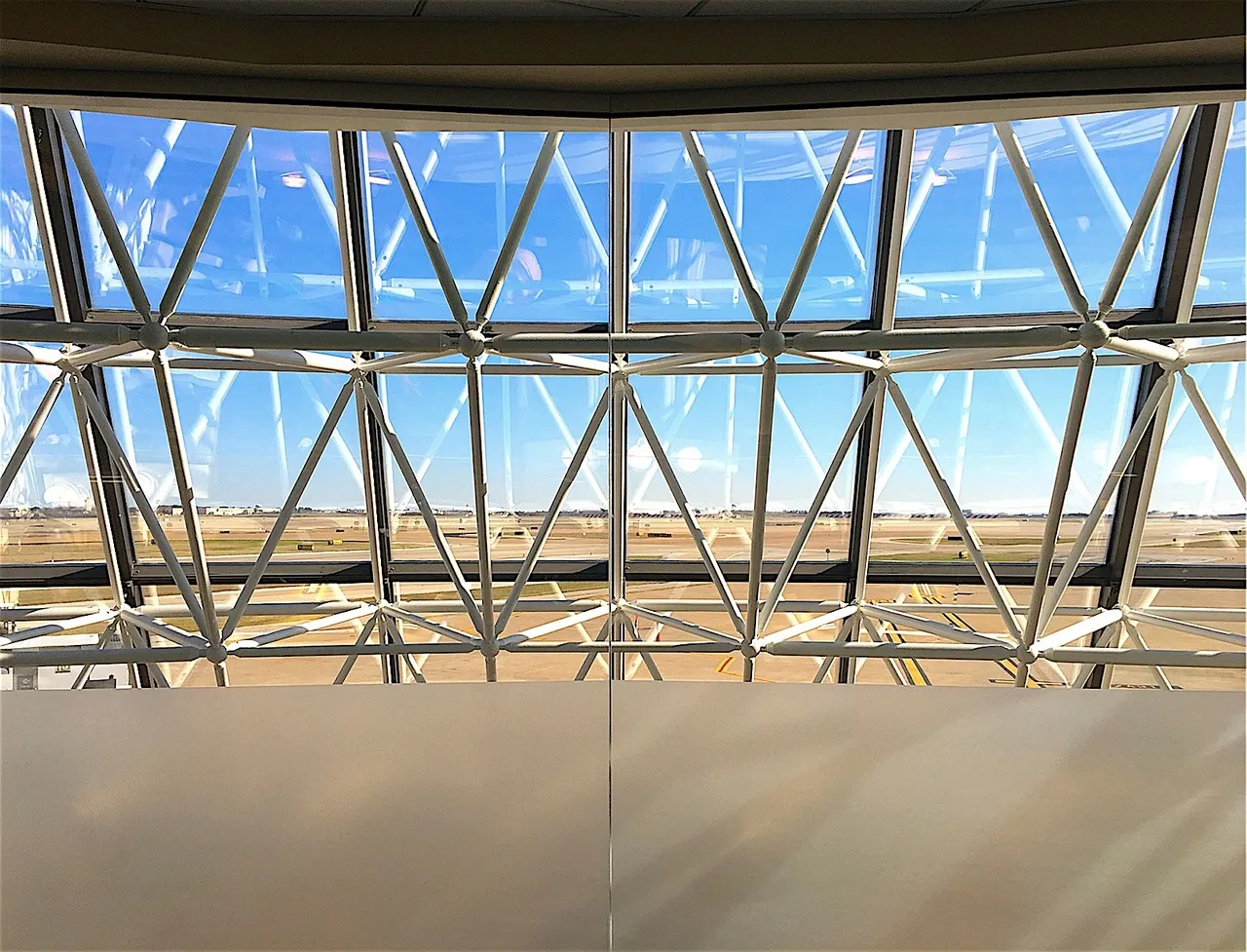 White steel lattice windows of an airport terminal, looking out over a sunlit airfield