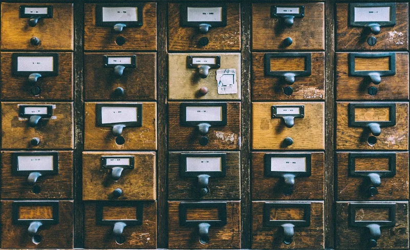 Rows of old wooden card-catalogue drawers, each with a small paper label and a metal pull