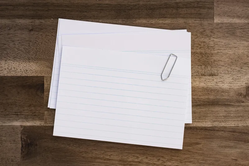 Three blank ruled index cards held with a paperclip, on a wooden desk