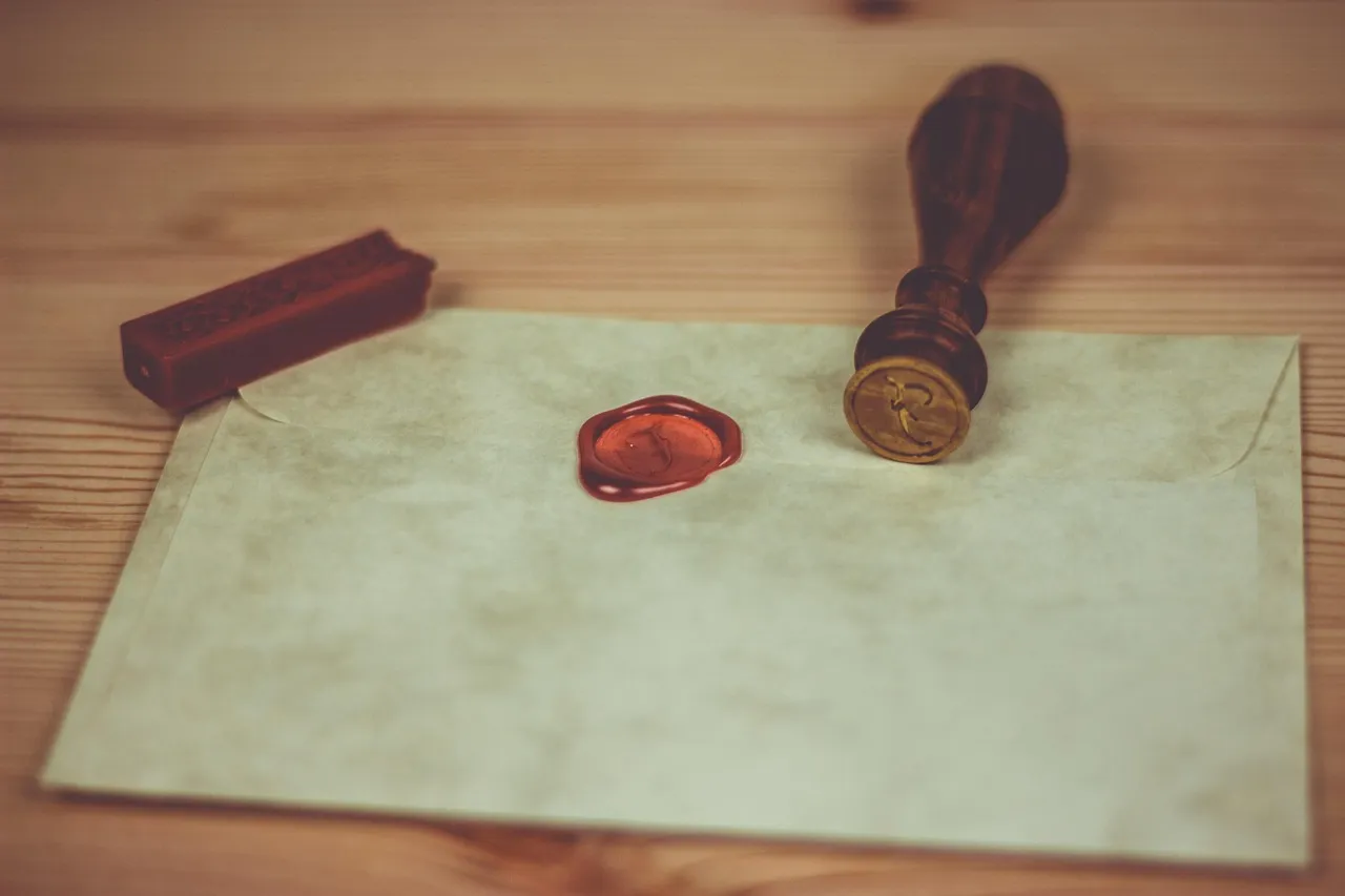 A cream envelope closed with a red wax seal, beside a wooden seal stamp and a stick of sealing wax