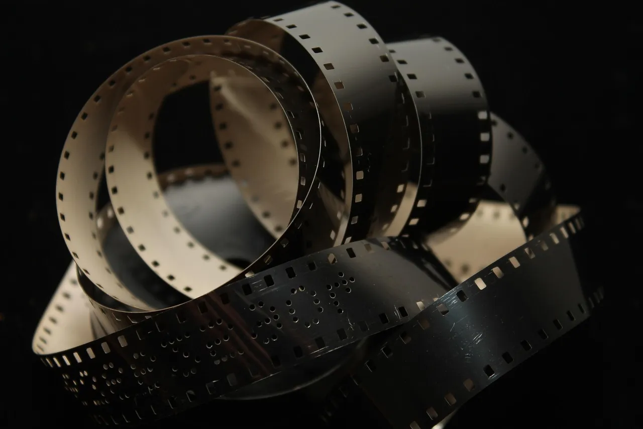 A loose coil of perforated film stock curling on a black background