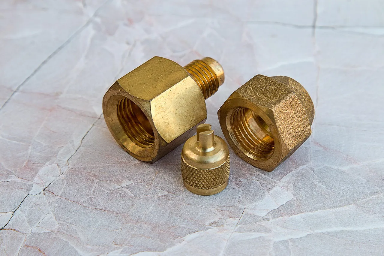 Three brass plumbing fittings, two threaded nuts and a small knurled cap, on a pale marble surface.