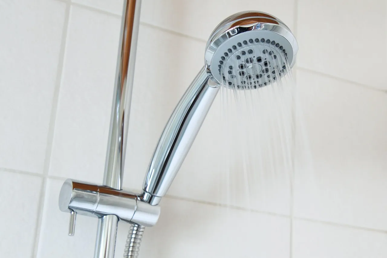 A chrome hand shower head running water, held in a bracket on a slide rail against white wall tiles.