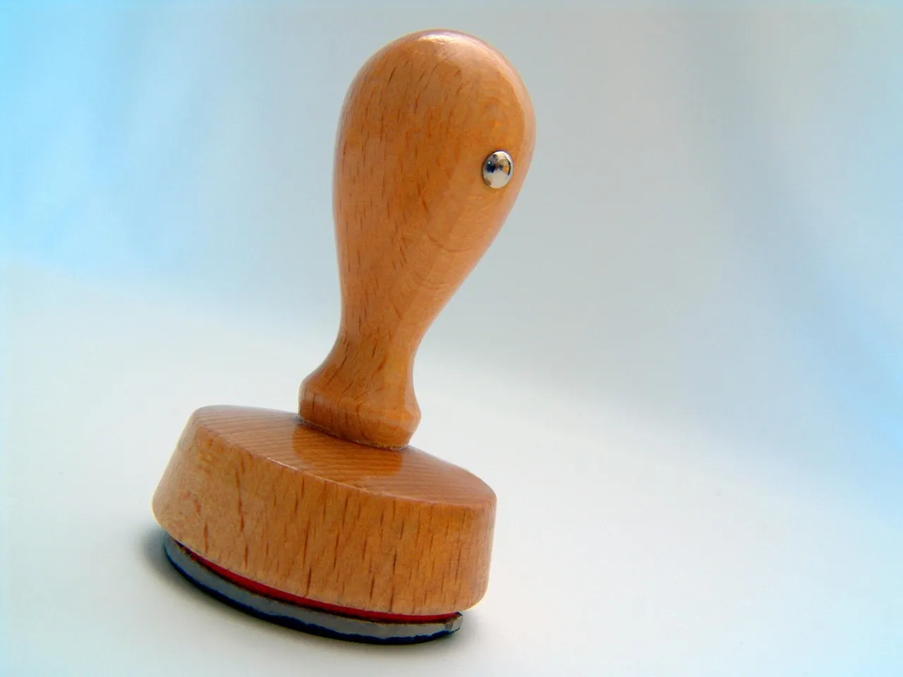 A wooden rubber stamp with a red pad, standing on a pale surface.