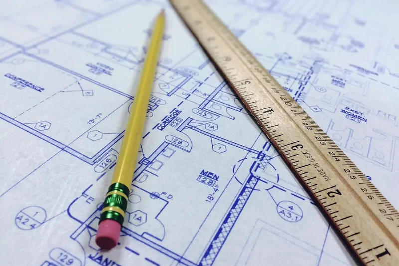 Blue architectural drawing sheets with a yellow pencil and a wooden ruler lying across them