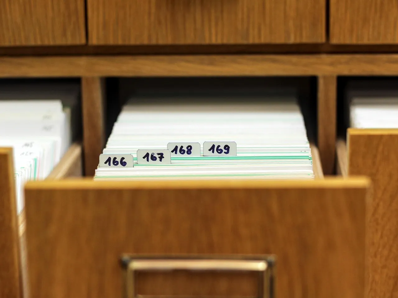 An open wooden drawer of white index cards, with numbered tabs sticking up at the front.