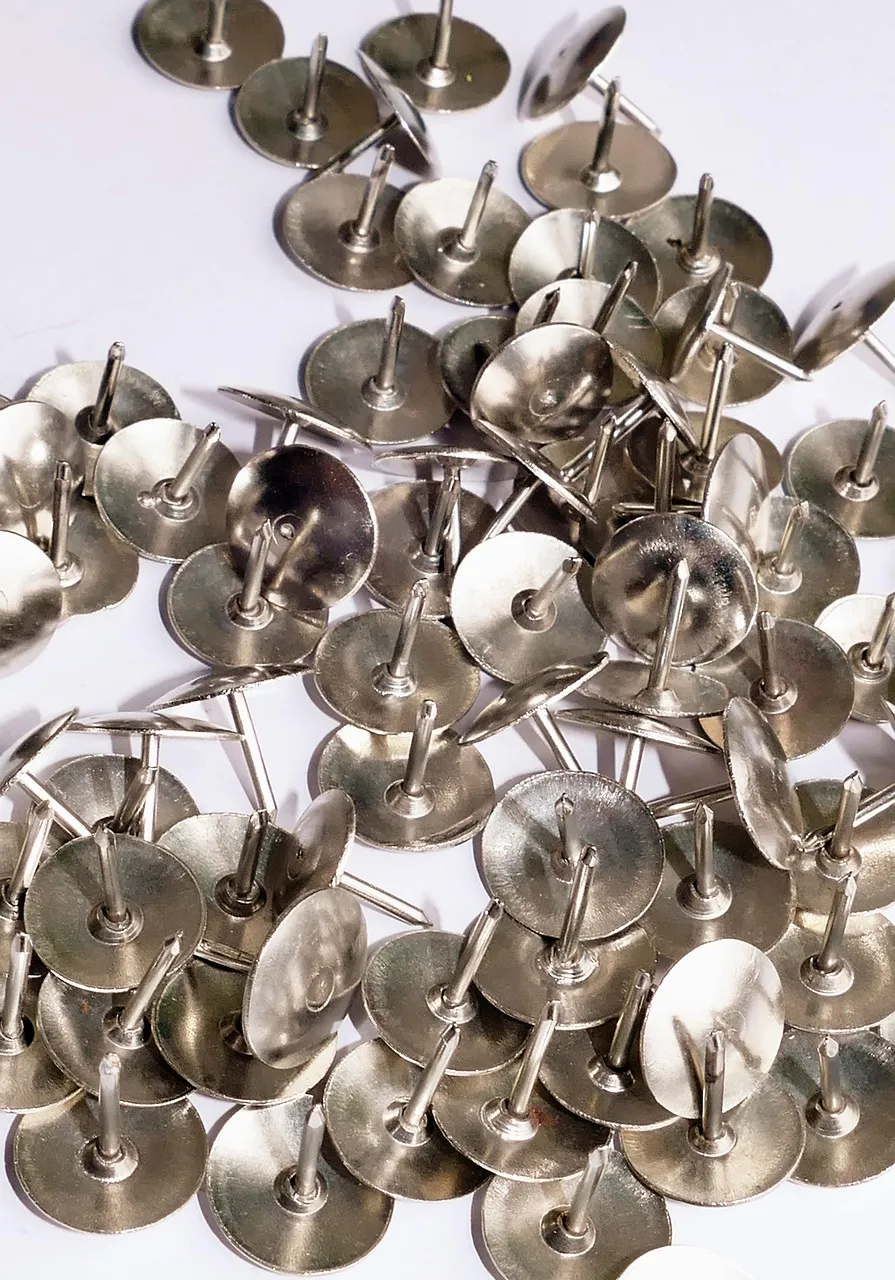 A heap of metal drawing pins on a white surface.