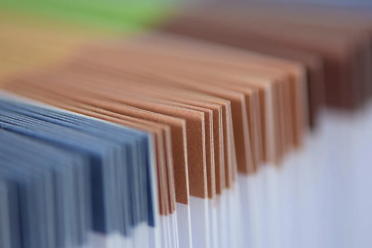 Close up, the edges of a stack of papers in blue, copper, green and yellow, sharp in the middle and soft at either end.