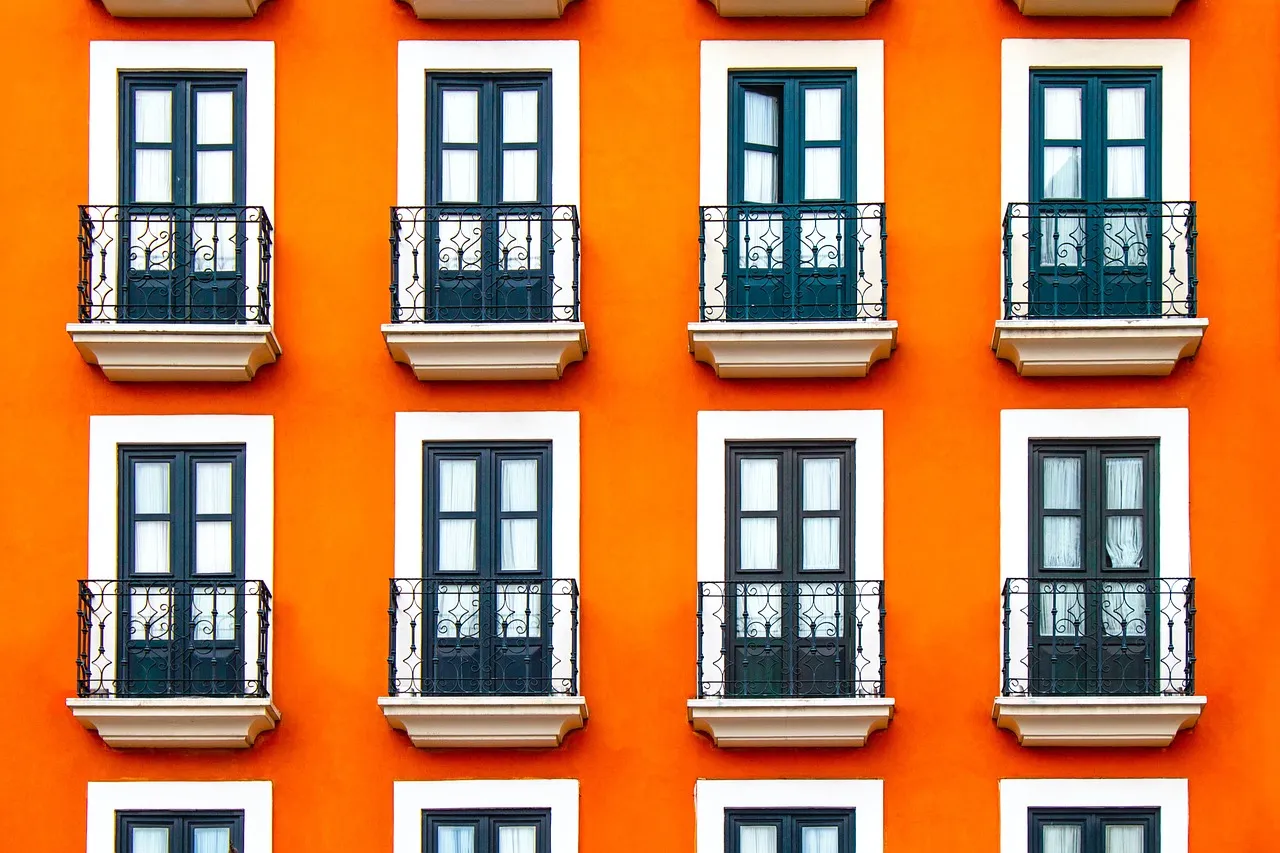 Rows of identical dark green double doors with small wrought-iron balconies on an orange apartment building