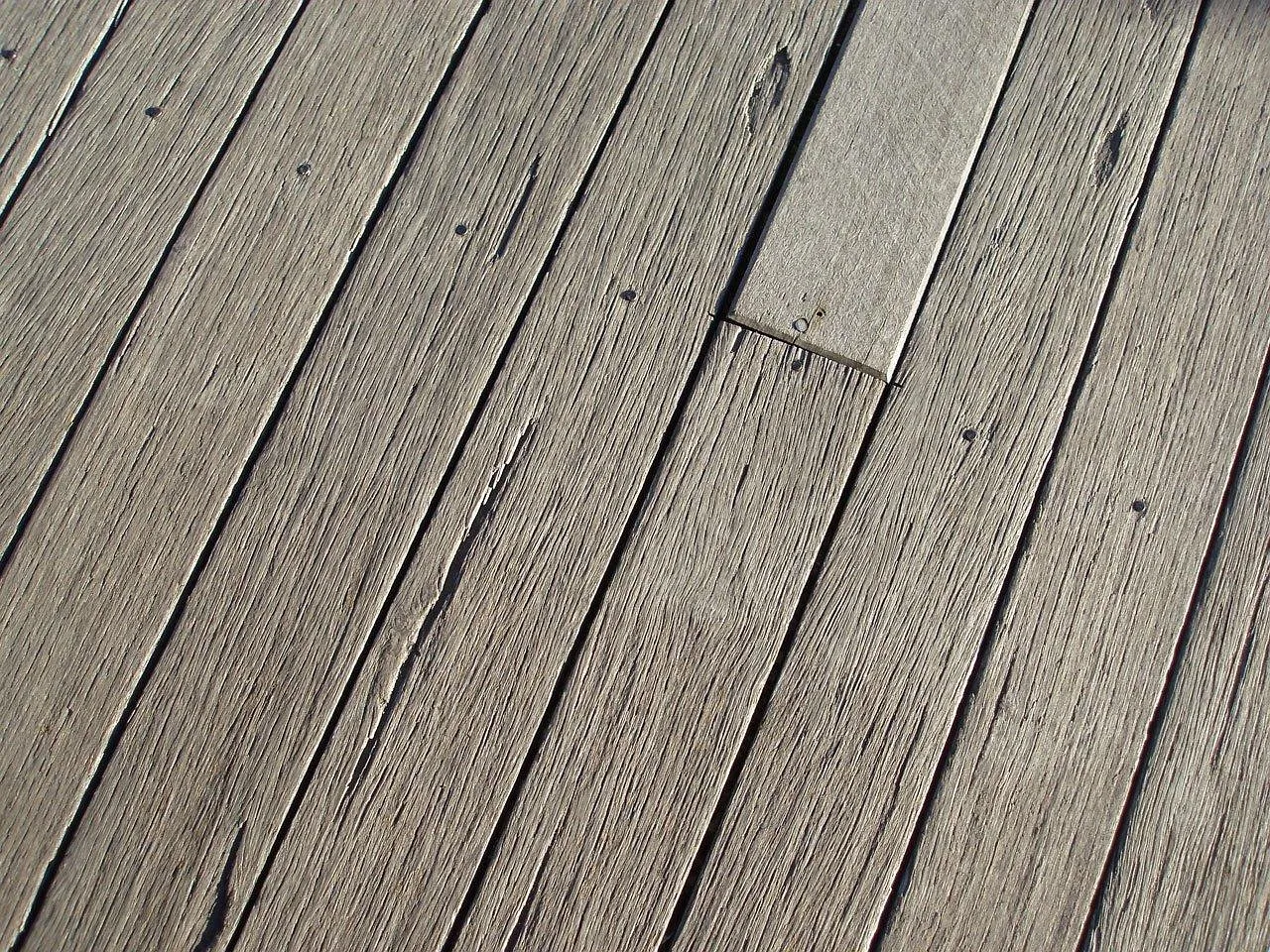 Weathered timber deck boards, silver grey, with fine surface checks, nail heads and one paler board let in